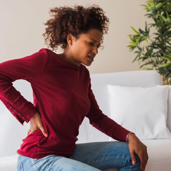 Young woman sitting in her couch, suffering from a back pain cramp.